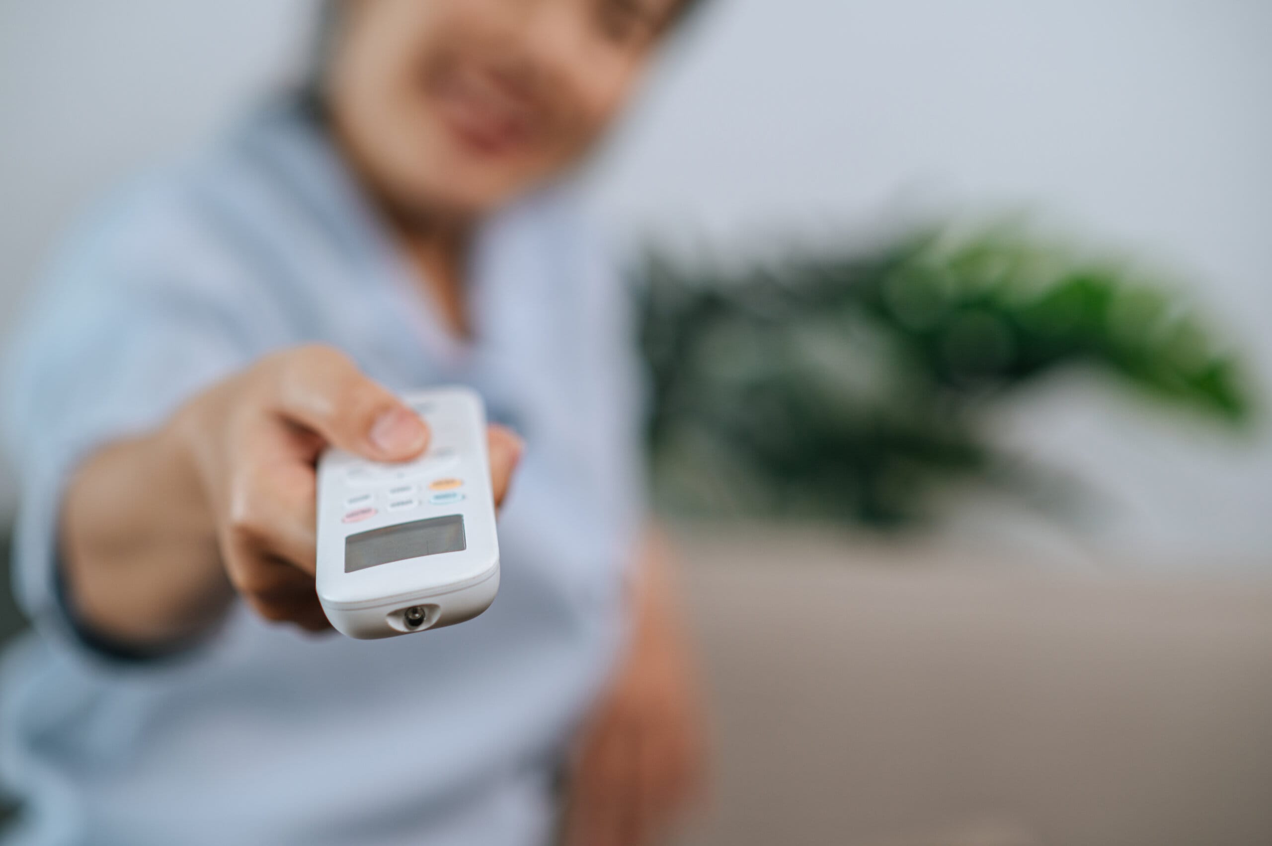 Young woman use romote control at home close up selective focus hand woman holding use remote control open aircondition living room home scaled